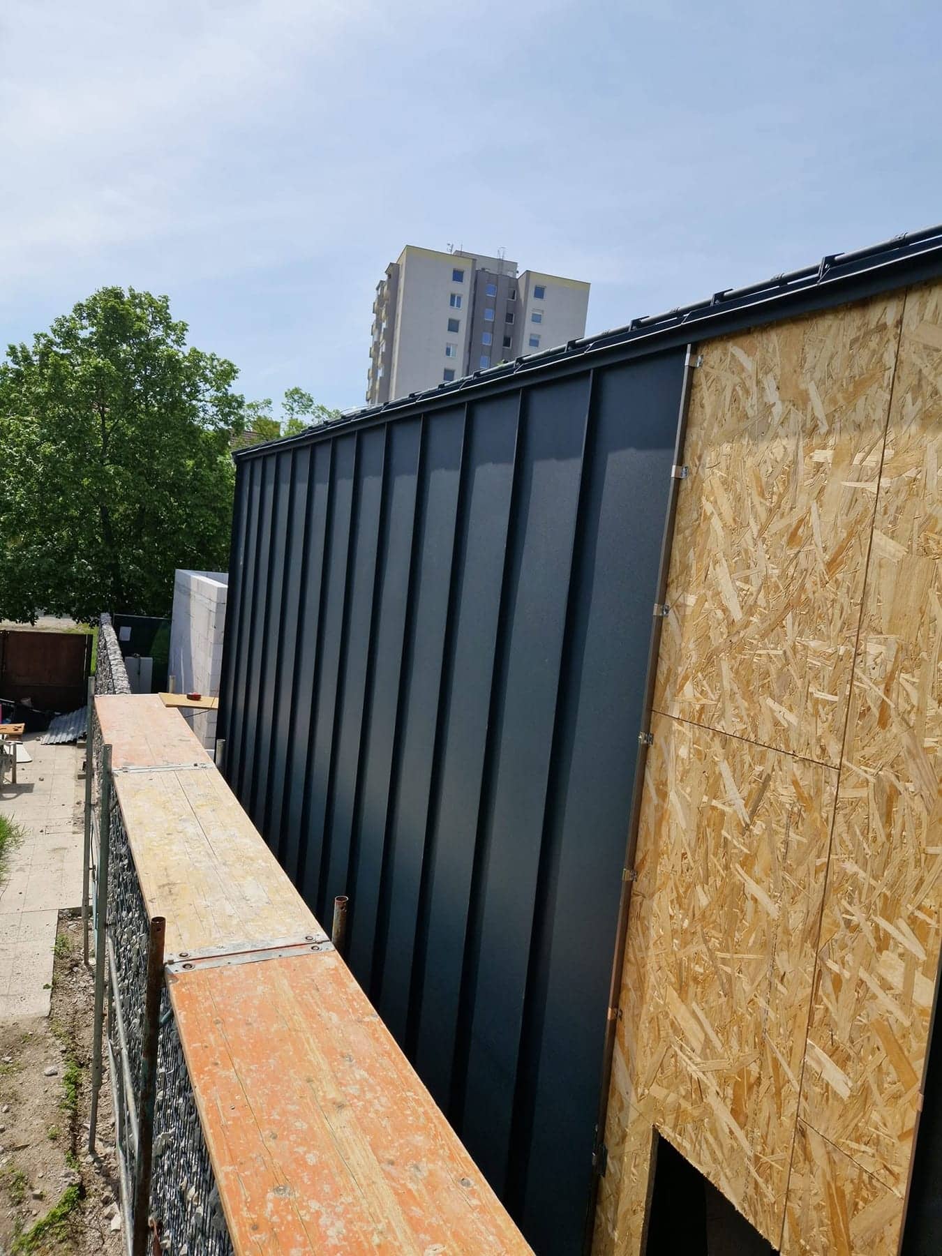 Antracitový falcovaný fasádny obklad novostavby počas montáže, Bratislava — BIRM